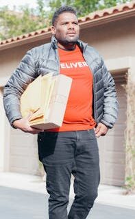 Professional courier delivering packages wearing a red shirt and black coat in a residential area.